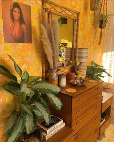 a room with a dresser, mirror and plants in front of yellow wallpapered walls