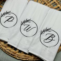 three white towels with black monogrammed font on them sitting in a wicker basket