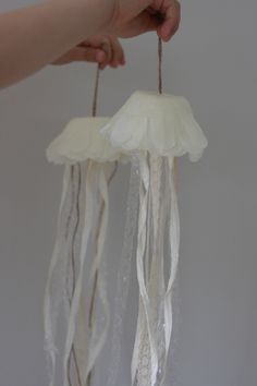 two white jellyfish hanging from strings in someone's hand on a gray background