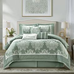 a bed with green comforters and pillows in a room next to a painting on the wall