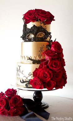 a three tiered cake with red roses on the bottom and black mask on top