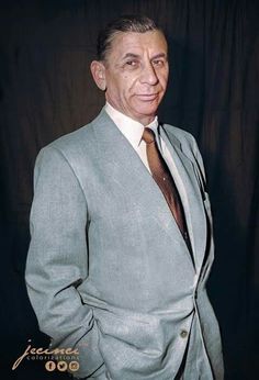 a man in a gray suit and tie posing for a photo with his hands in his pockets