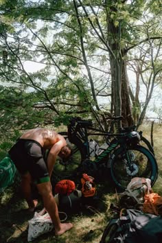 a man standing next to a bike in the woods with backpacks on it's back