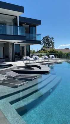 an outdoor swimming pool with lounge chairs next to it and a house in the background