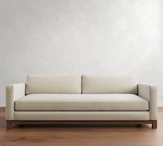 a white couch sitting on top of a hard wood floor next to a gray wall