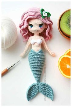 a crocheted mermaid doll sitting next to an orange and kiwi fruit slice