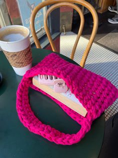 a pink knitted purse sitting on top of a table next to a cup of coffee