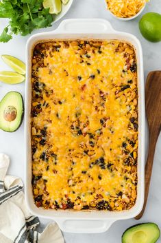 an enchilada casserole in a white dish with avocado, cilantro and limes around it