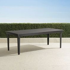 an outdoor dining table in the middle of a concrete patio area with hedges behind it