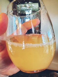 a person holding up a wine glass filled with liquid and an orange slice in it