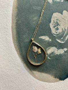 a necklace with a rose in it on top of a piece of paper next to a painting