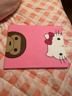 a pink canvas with a hello kitty and dog on it sitting on a checkered bedspread