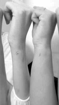 two women with matching tattoos on their arms, one is holding the other's arm