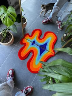 a person standing next to a colorful rug on the floor with a cat looking at it