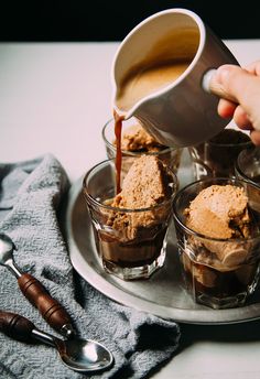 someone pouring ice cream into small cups on a silver platter with spoons next to it