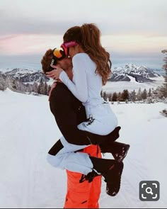 a man holding a woman on his back while standing in the snow with mountains in the background