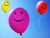 three balloons with smiley faces flying in the sky