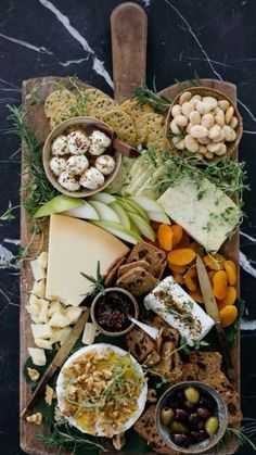 an assortment of cheeses, crackers and olives on a wooden platter