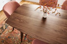 a wooden table with chairs around it and a vase filled with flowers in the middle