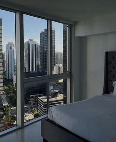 a bed sitting next to a window in a room with tall buildings on the other side