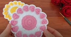 two crocheted coasters in the shape of flowers on a table with red roses