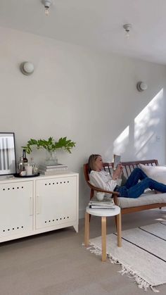 a woman laying on a bed in a room with white walls and flooring, while reading a book