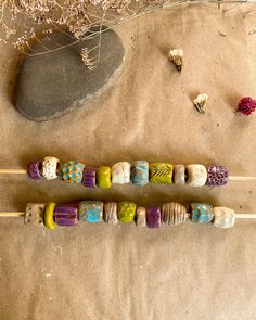 several different colored beads on sticks next to some rocks and dried flowers in the background