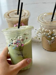 three iced drinks with flowers in them are being held up by someone's hand