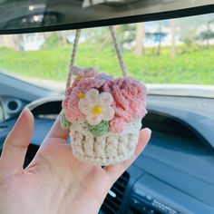 a hand is holding a small crocheted basket with flowers on the front and side