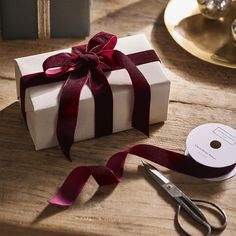 a gift wrapped in white paper with a red ribbon next to scissors on a table