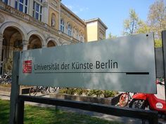 a large sign in front of a building with bicycles parked outside it and people walking by