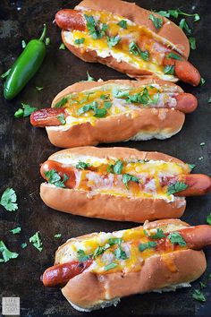 three hot dogs on buns covered in cheese and ketchup, with green garnish