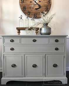 an old dresser is painted gray and has a large clock on it's face