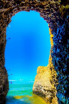 an ocean cave with water and rocks in the foreground, under a blue sky