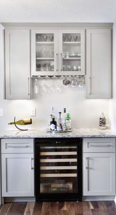 a wine cooler in the middle of a kitchen with white cabinets and wood flooring