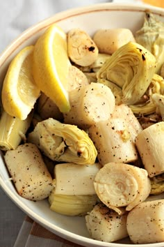 a white bowl filled with sliced artichokes and lemon wedges on top of a table