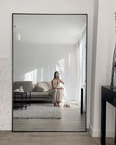 a woman is sitting on the floor in front of a mirror that reflects her living room