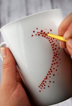 a person is holding a coffee cup with red beads on it and a pencil in their hand