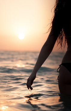 a woman standing in the ocean at sunset with her hand on the water's edge