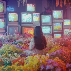 a woman sitting in the middle of flowers watching tvs on television's behind her