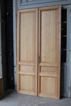 two large wooden doors in a room with concrete flooring and walls behind them,