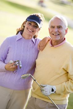 an older man and woman posing for the camera while holding golf clubs