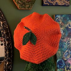 an orange knitted hat sitting on top of a wooden table next to paintings and mirrors