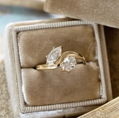 an engagement ring with two pear shaped diamonds in a box on top of carpeted floor