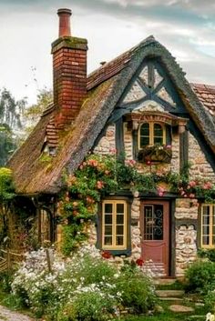 an old cottage with flowers growing on the roof