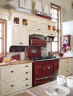 a red stove top oven sitting inside of a kitchen next to white cabinets and drawers