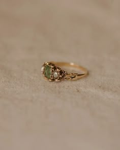 a gold ring with two green stones on the front and one stone in the back