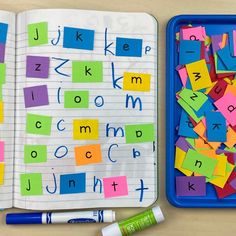 an open book with letters and numbers on it next to a blue container filled with crayons