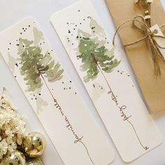 two bookmarks with watercolor trees on them next to a christmas ornament