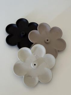 three flower shaped plates sitting on top of a white table next to an orange and black one